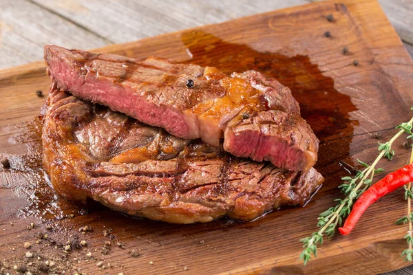 Cut Rib eye steak on wooden board, closeup. Rib eye steak on wooden board decorated with chili pepper and thyme