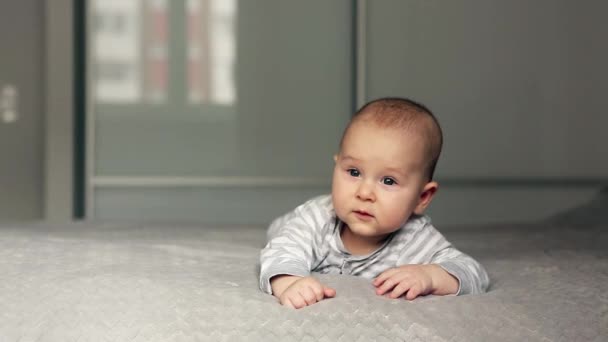 Un bebé precioso yace en la cama y mira a la cámara — Vídeos de Stock