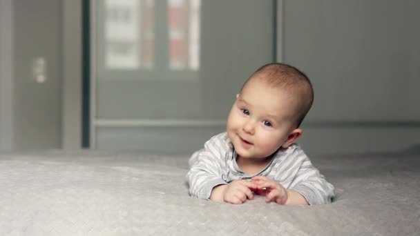 Χαριτωμένο μωρό ξαπλώνει στο κρεβάτι κοιτάζοντας στην κάμερα και χαμογελώντας — Αρχείο Βίντεο