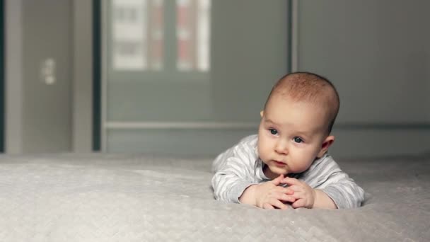 Een prachtige kleine baby ligt op het bed en kijk naar de camera — Stockvideo