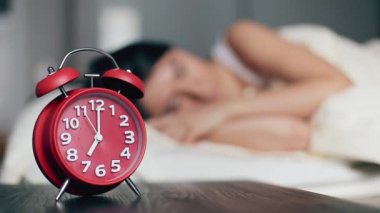 Komodinin üzerindeki çalar saat, uyuyan kadının arka planına karşı. 