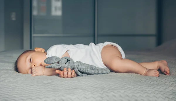 Γλυκό νεογέννητο μωρό κοιμάται με ένα γκρι λαγό παιχνίδι στο κρεβάτι — Φωτογραφία Αρχείου