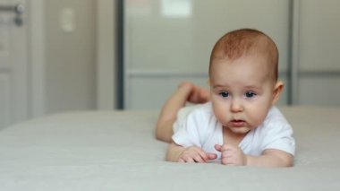 Sevimli bebek yatağa uzanıp kameraya bakıyor ve gülümsüyor.