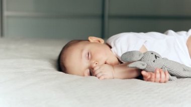Elinde gri bir tavşanla battaniyenin üzerinde uyuyan tatlı bir çocuk.