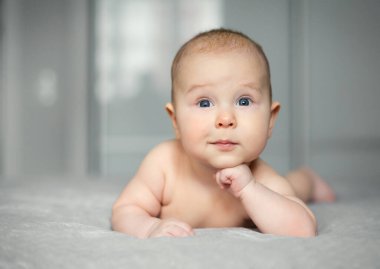 Güzel gülümseyen oğlan gri battaniyeye uzanıp poz veriyor.