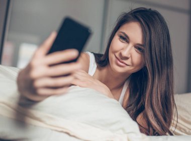 Yatağa uzanıp selfie çeken tatlı bir genç kadın.