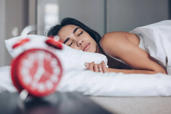 Jovem dormindo na cama. Relógio de alarme vermelho em primeiro plano — Fotografia de Stock