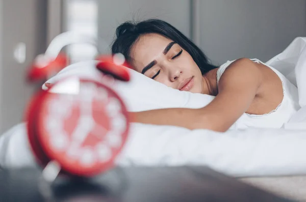 Genç bir kadın yatakta uyuyor. Ön planda kırmızı alarm saati — Stok fotoğraf