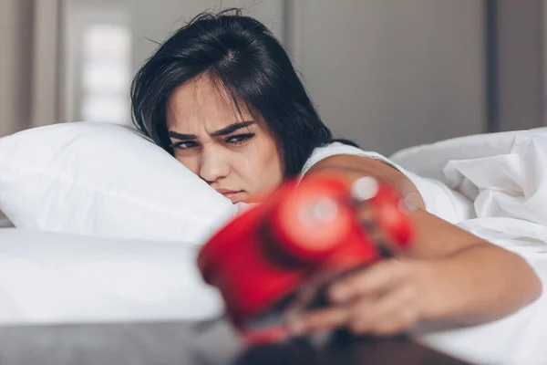 Vakna upp av ung sömnig arg kvinna stoppa väckarklocka på sängen — Stockfoto