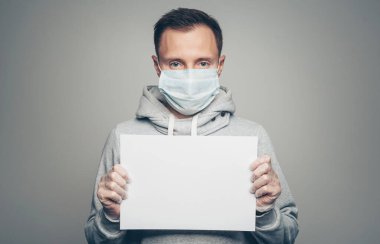 Stüdyo portresi, maske takan ve eldivenleri boş olan gri arka plandaki kameraya bakan genç erkeklerin portresi. Koronavirüs salgını, toz alerjisi, virüse karşı koruma