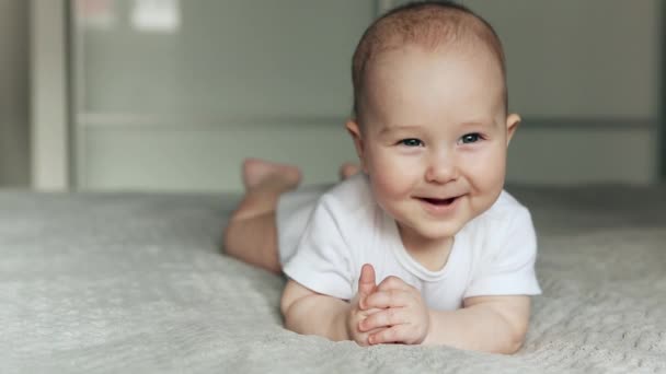 Leuke baby ligt op bed kijkend in de camera en glimlachend — Stockvideo