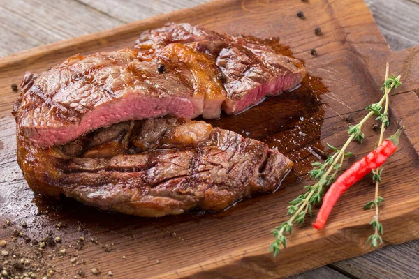 Couper un steak aux côtes levées sur une planche en bois, gros plan. Steak côtelé sur planche de bois décorée de piment — Photo