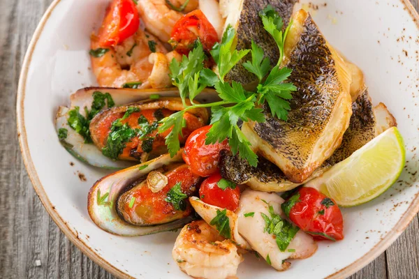 Mix of fish, mussels, clams, shrimps and tomatoes with lime on wooden background — Stock Photo, Image