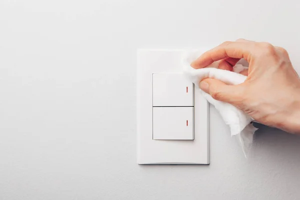 Vista de cerca de la mano de la mujer usando una toallita húmeda antibacteriana para desinfectar el interruptor eléctrico de la habitación en la pared gris —  Fotos de Stock