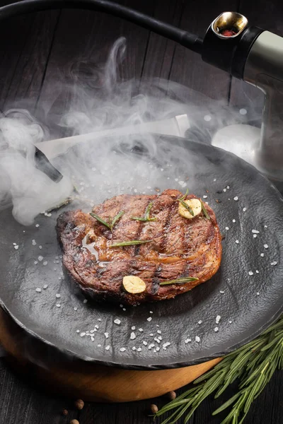 Steak de boeuf fumé avec des herbes sur une assiette noire. Pistolet fumeur et steak de viande. Technologie moderne de préparation — Photo