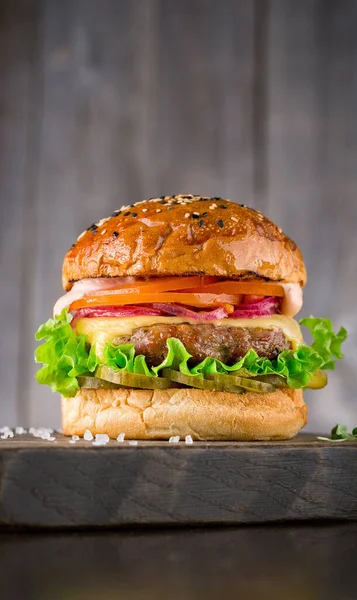 Ízletes burger marhahússal, paradicsommal, pácolt, hagymával, sajttal, salátával és mártással fa alapon Jogdíjmentes Stock Fotók