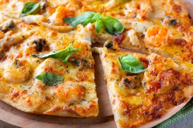 Karides, midye ve ahşap arka planda fesleğenli ince deniz ürünleri pizzası.