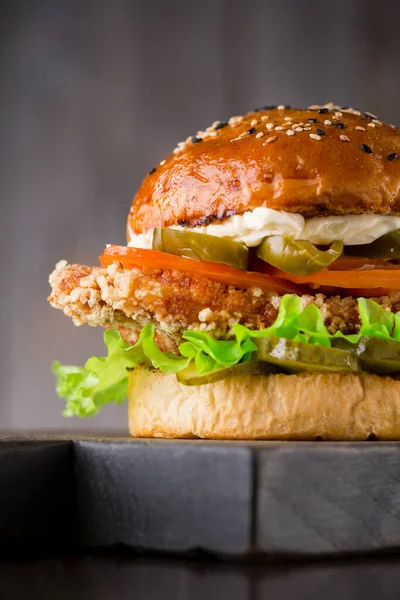 Chutný burger s hovězím masem, rajčaty, nakládanou zeleninou, paprikou jalapeno, salátem a omáčkou na dřevěné desce na dřevěném pozadí s kopírovacím prostorem — Stock fotografie