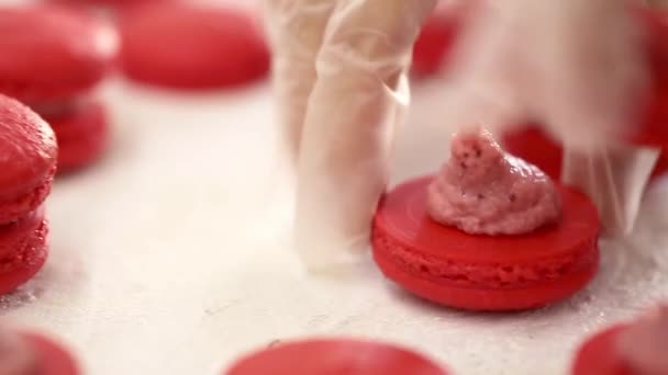 Rode Macarons aan het maken. Close-up shot van het verbinden van twee helften macarons met aardbeiencrème — Stockvideo