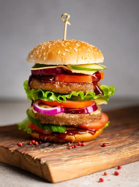 Big royal gustoso hamburger, hamburger, cheeseburger con due costolette, pomodori, cetriolo, insalata, cipolla, formaggio e salsa su tagliere di legno su sfondo grigio — Foto Stock