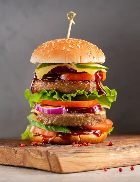 Big royal gustoso hamburger, hamburger, cheeseburger con due costolette, pomodori, cetriolo, insalata, cipolla, formaggio e salsa su tagliere di legno su sfondo scuro — Foto Stock