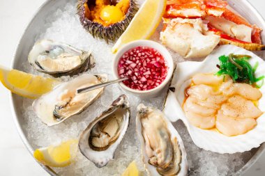 Buzlu taze deniz ürünleriyle dolu büyük bir tabak. İstiridye, kirpi, istiridye ve yengeç. Limon dilimi ve soslu deniz ürünleri manzarasını kapat. Restoranda ezilmiş buzlu deniz mahsulleri.