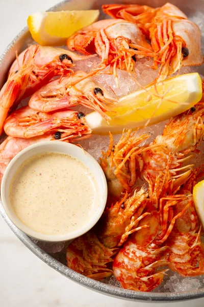 Freshly cooked assorted shrimps on the ice plate with lemon slices and sauces on a stone countertop. — Stock Photo, Image