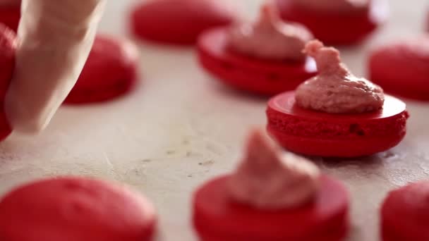 Faire des macarons rouges. Gros plan sur la connexion de deux moitiés de macarons à la crème aux fraises 