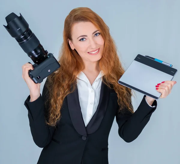 Young redhead woman holding a camera and a tablet for graphic design.