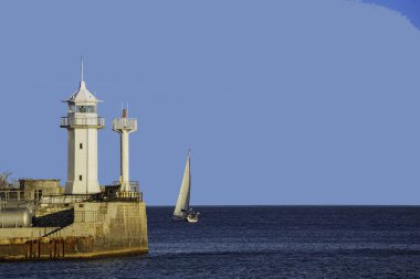 Karadeniz 'deki beyaz deniz feneri, bir yelkenli teknesi körfezden denize doğru hareket ediyor.