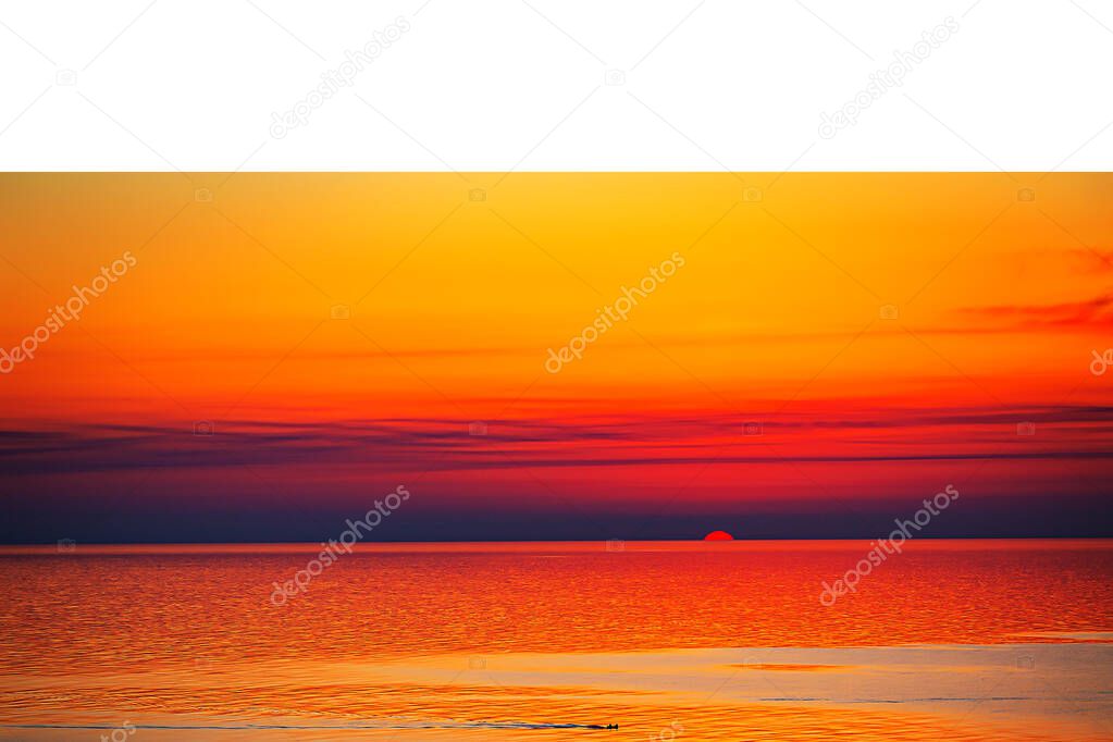 The sun is sinking into the sea and a crimson sunset has filled the entire sky. The sea is calm and quiet, reflecting the bright colors of the sky.