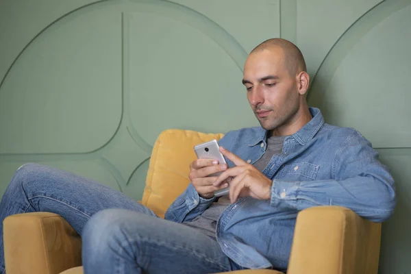 Man sitting in armchair and reading message on his mobile phone