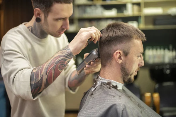 Barber using electric razor while providing a haircut for male customer at barber shop