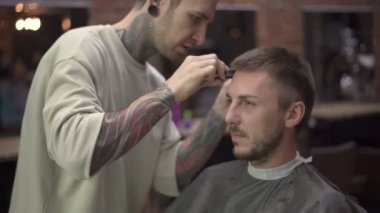 Berber, berber dükkanında erkek müşteriye tıraş olurken elektrikli tıraş makinesi kullanıyor.