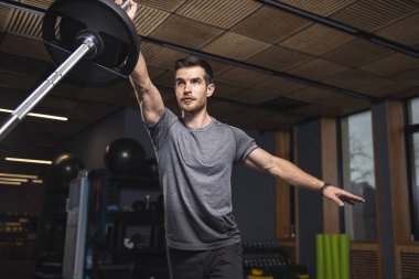 Genç adam spor salonunda ağırlık çalışıyor halterle egzersiz yapıyor.