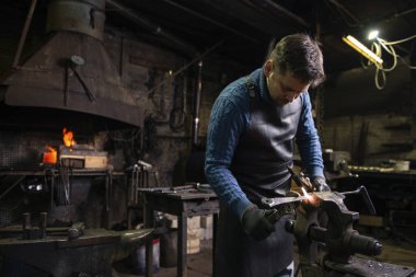 Erkek demirci atölyesinde metali alevler içinde ısıtıyor.