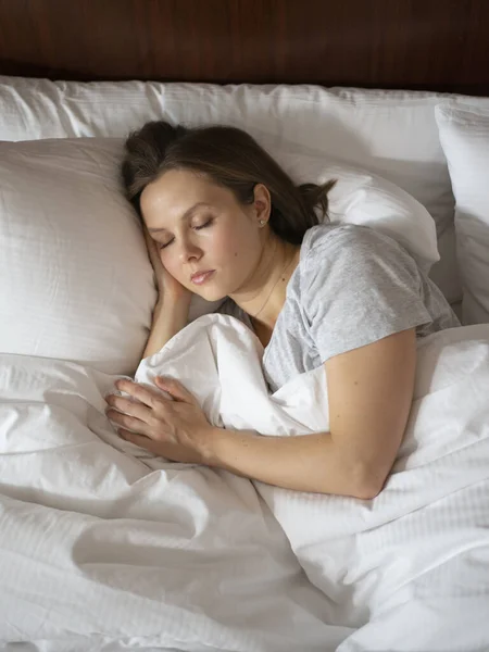 Woman cozily sleeping in bed putting her hand under head