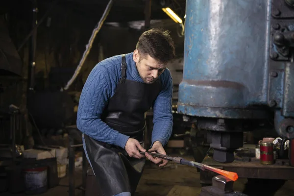 Blacksmith forging hot metal with hammer at anvil in blacksmith shop