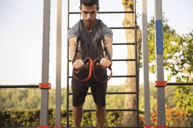 Spor yapan genç adam dışarıda spor aletleriyle egzersiz yapıyor.