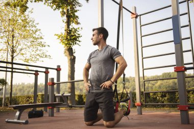 Spor yapan genç adam dışarıda spor aletleriyle egzersiz yapıyor.