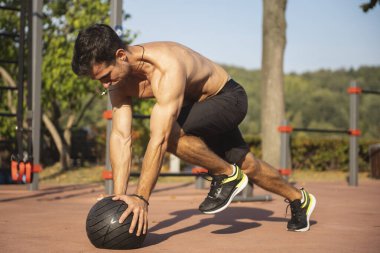 Açık havada top kullanarak egzersiz yapan formda bir adam. Şehir parkında genç sporcu eğitimi.