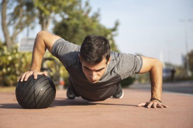 Açık havada top kullanarak egzersiz yapan formda bir adam. Şehir parkında genç sporcu eğitimi.