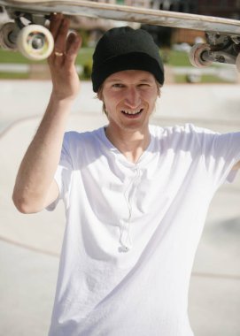 Kaykaylı neşeli genç adam kameraya bakıyor ve gülümsüyor.