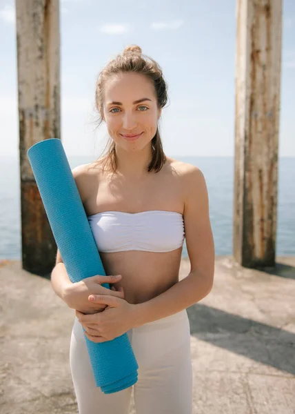 Mujer Joven Sonriente Sosteniendo Esterilla Yoga Mientras Está Pie Muelle Fotos de stock libres de derechos