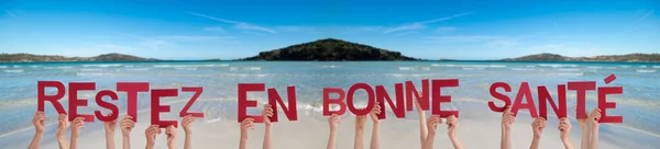 Emberek kezében Restez En Bonne Sante azt jelenti, maradj egészséges, Ocean Háttér — Stock Fotó