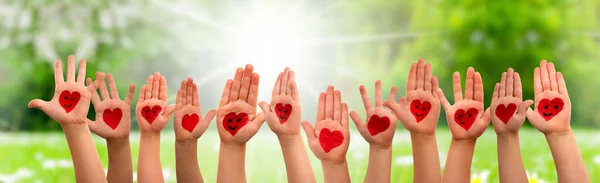 Mains d'enfants avec le symbole de coeur et les sourires, prairie d'herbe comme fond — Photo