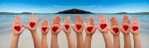 Las manos de los niños con el símbolo del corazón y emoticonos, el océano y la playa como fondo —  Fotos de Stock