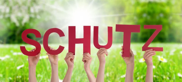Les gens mains tenant le mot Schutz signifie protection, prairie d'herbe — Photo