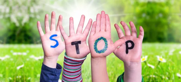 Las manos de los niños sosteniendo la palabra Stop, prado de hierba — Foto de Stock