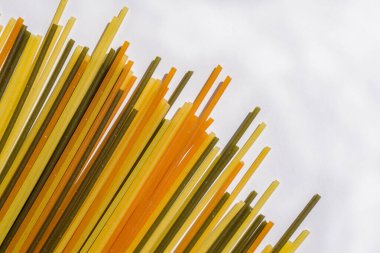 Beyaz arka planda köşegen sıra halinde çok renkli makarna. Ispanaklı ve havuçlu makarna. İtalyan yemeği kavramı. Logo veya metin için boşluk kopyala.